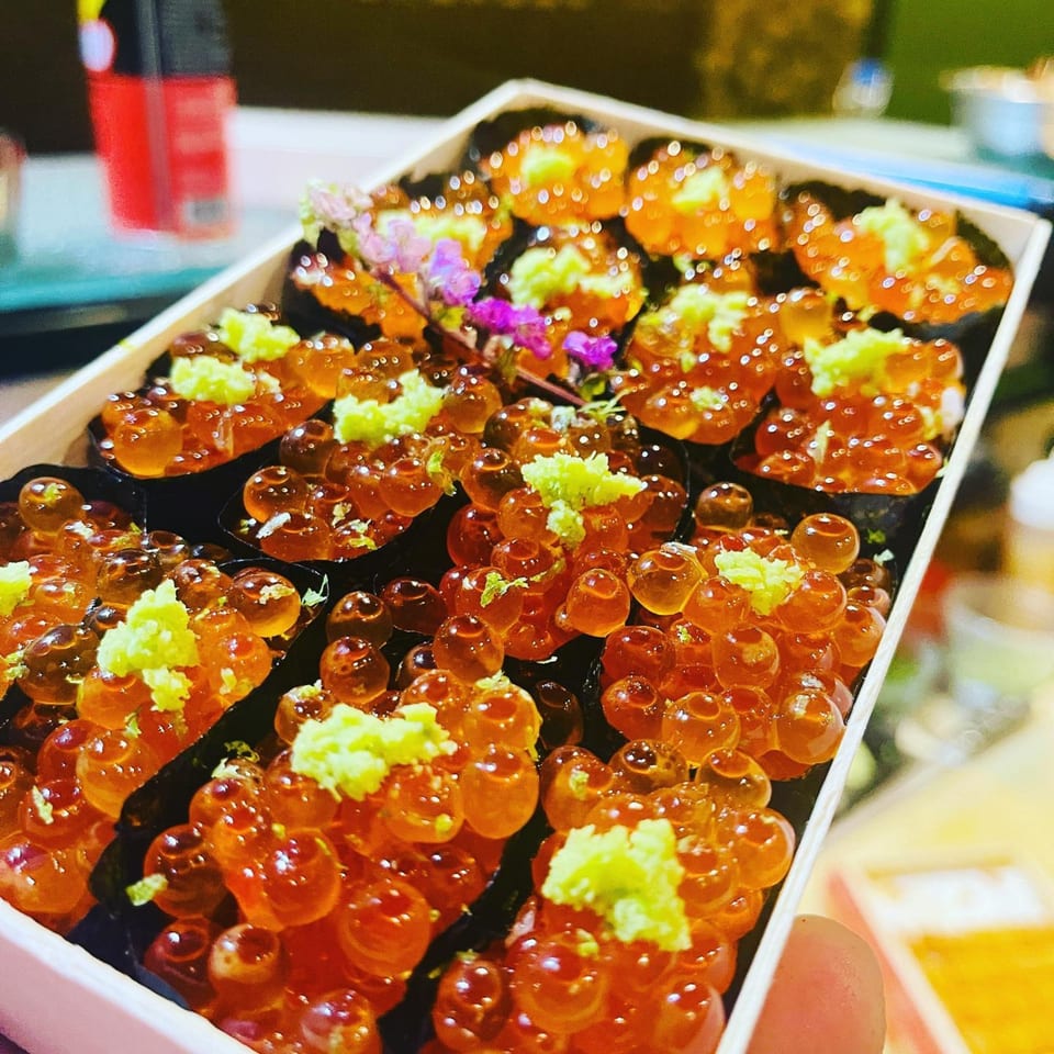 Close-up of a box of Sushi Hatsune ikura gunkan sushi, topped with bright green grated ginger.