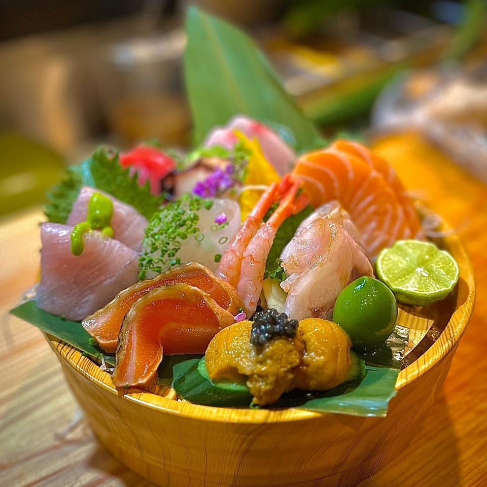 A wooden bowl filled with various sashimi, including salmon, shrimp, uni, and caviar, garnished with lime.