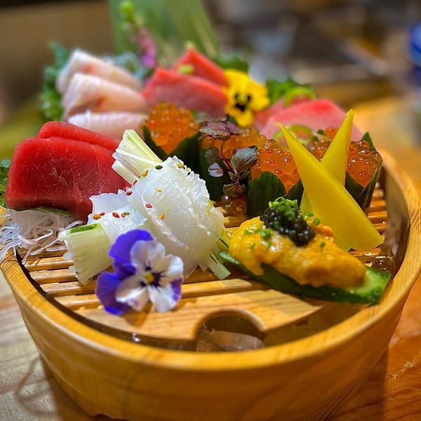 A wooden boat filled with various colorful sushi and sashimi, garnished with flowers.